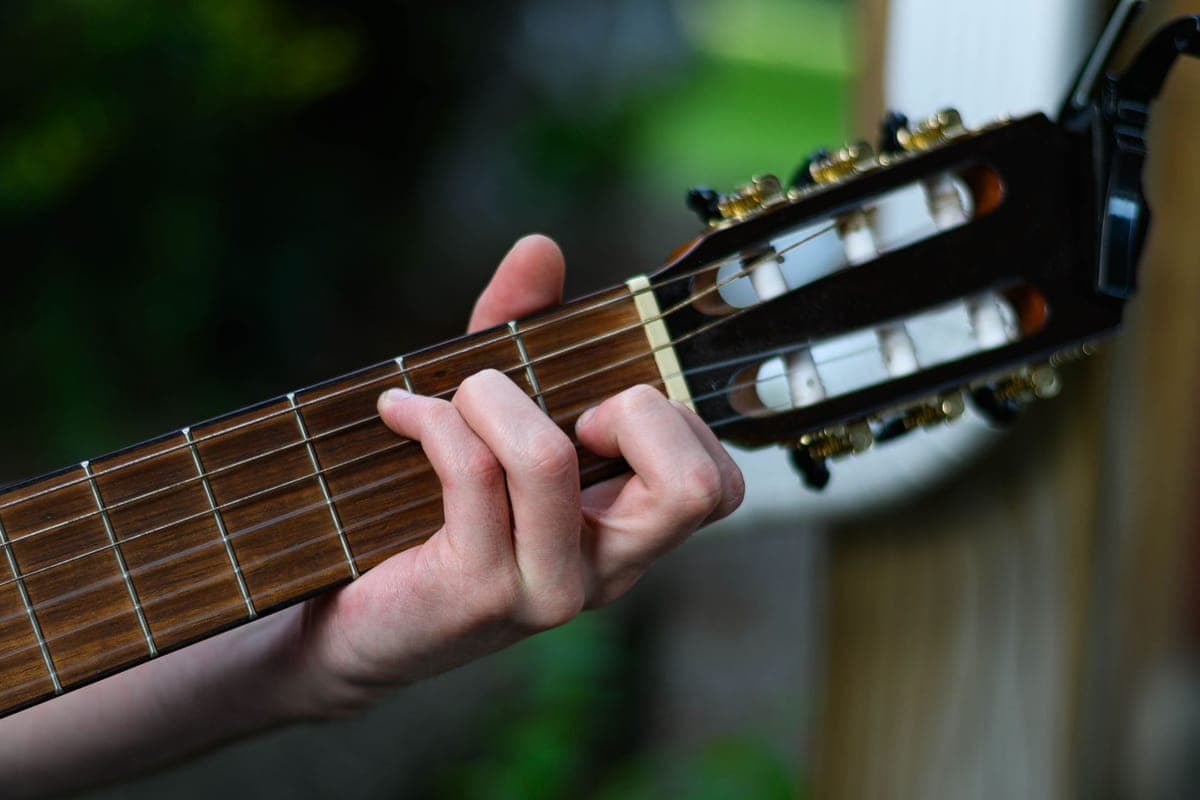 A hand fretting a chord on the wide neck of a classical guitar