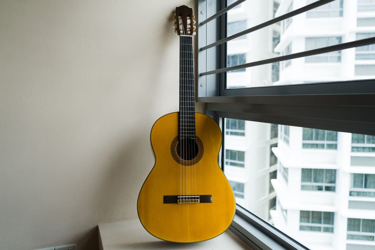 A classical guitar leaning against a window in a bright room