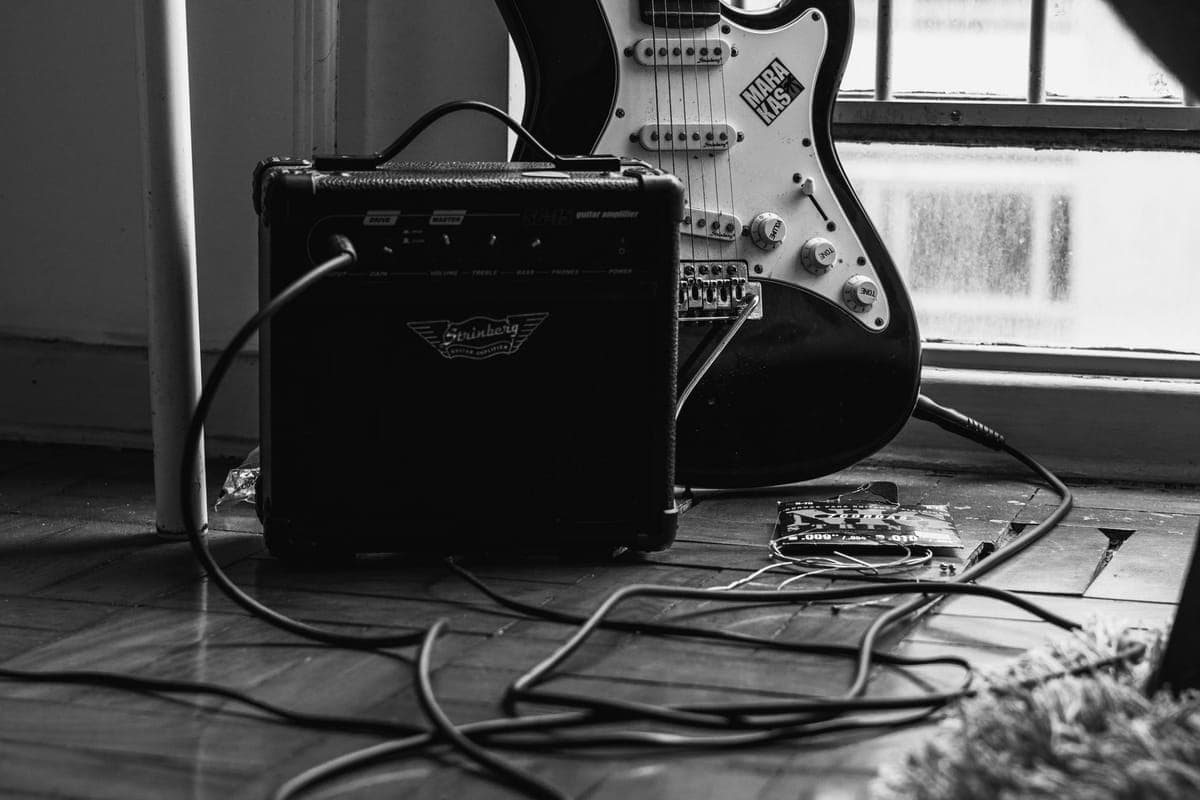 An electric guitar with a cable and a small practice amplifier