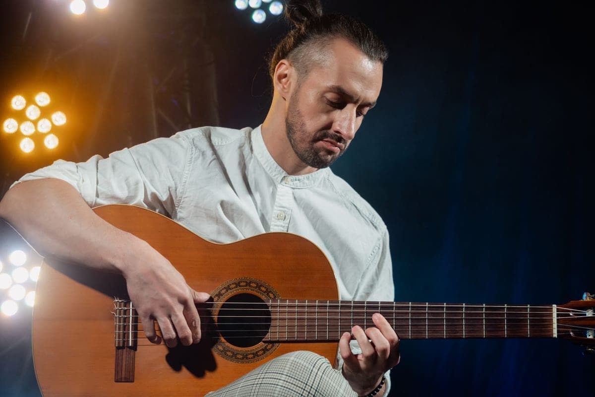 A guitarist seated with a classical guitar raised on his leg