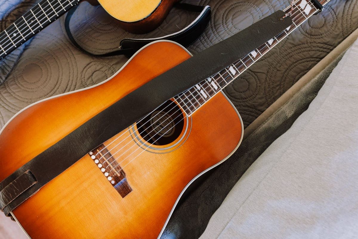 An acoustic guitar with a strap laid across a textured bedspread