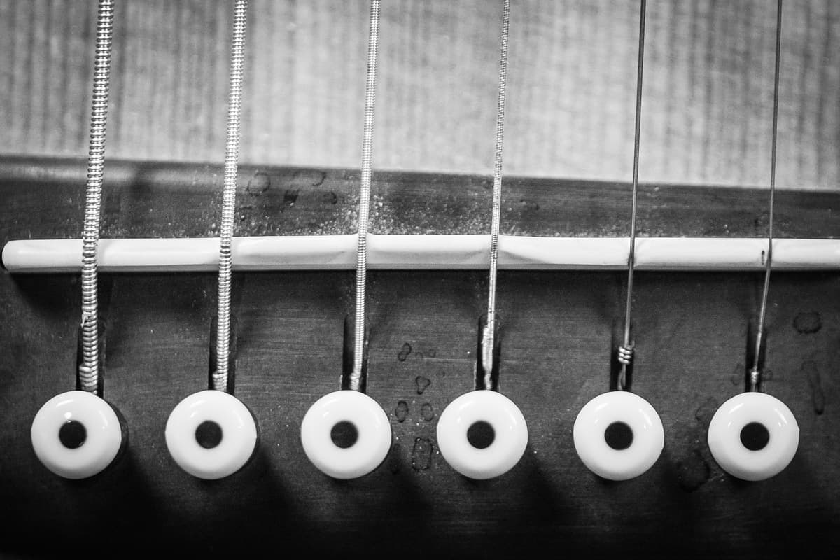 A black and white close-up of an acoustic guitar's strings and bridge