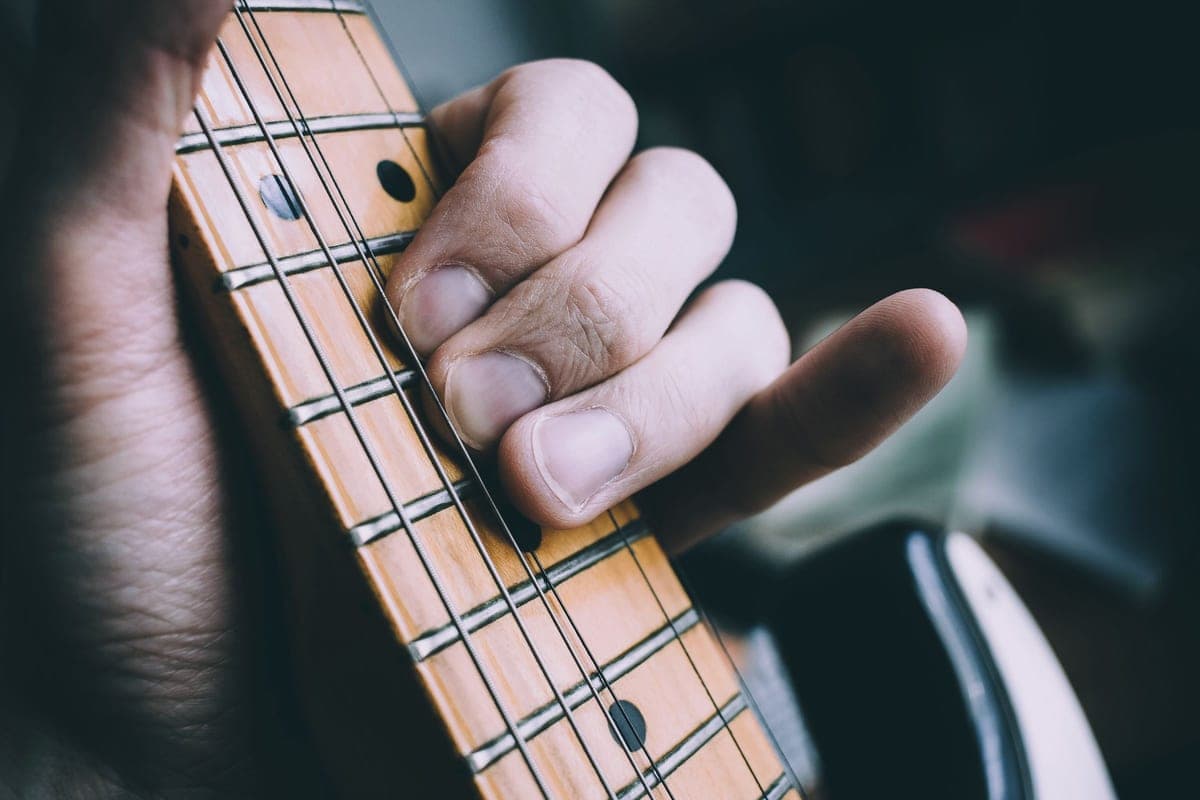 A hand playing notes on an electric guitar fretboard