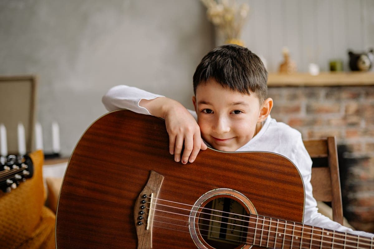 A smiling child holding an acoustic guitar indoors