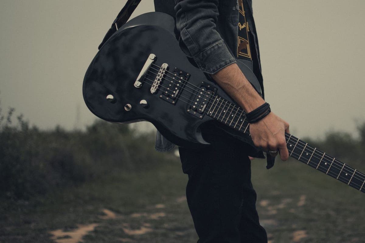 A guitarist holding a black electric guitar, strings and fretboard in view