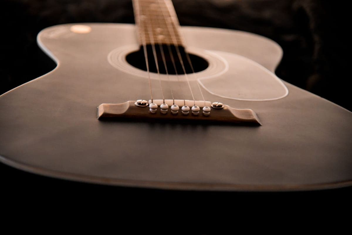 A set of bronze acoustic guitar strings beside an acoustic guitar