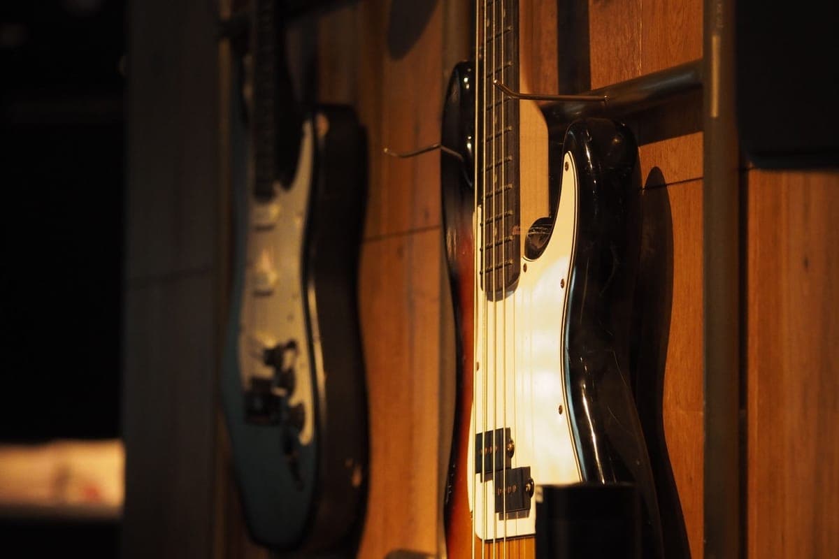 A guitar on a wall hanger beside a guitar in a floor stand