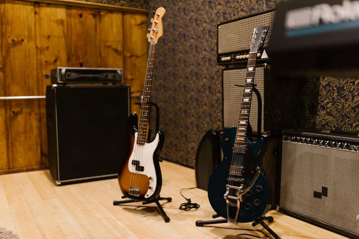 A guitar resting in a floor stand beside a wall-mounted hanger
